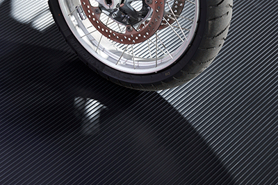 Ribbed texture in midnight black shown with a partial view of a motorcycle tire and wheel on the mat