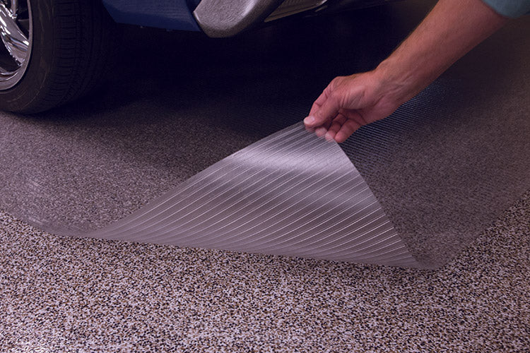 Clear Ribbed flooring with hand lifting up the corner to show transparency and there is a small portion of a vehicle shown on the mat for illustrative purposes