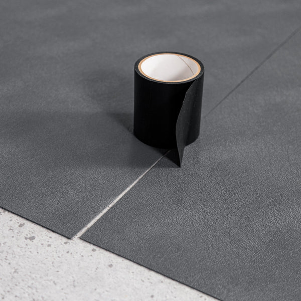 Roll of black seam tape on top of two pieces of Slate Grey Levant texture vinyl flooring