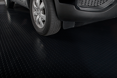 Large Coin Texture in midnight black garage mat shown in partial view with a front quarter view of a car on the mat