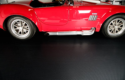small coin texture garage mat in midnight black shown with a partial view of a red sports car on the mat for illustrative purposes